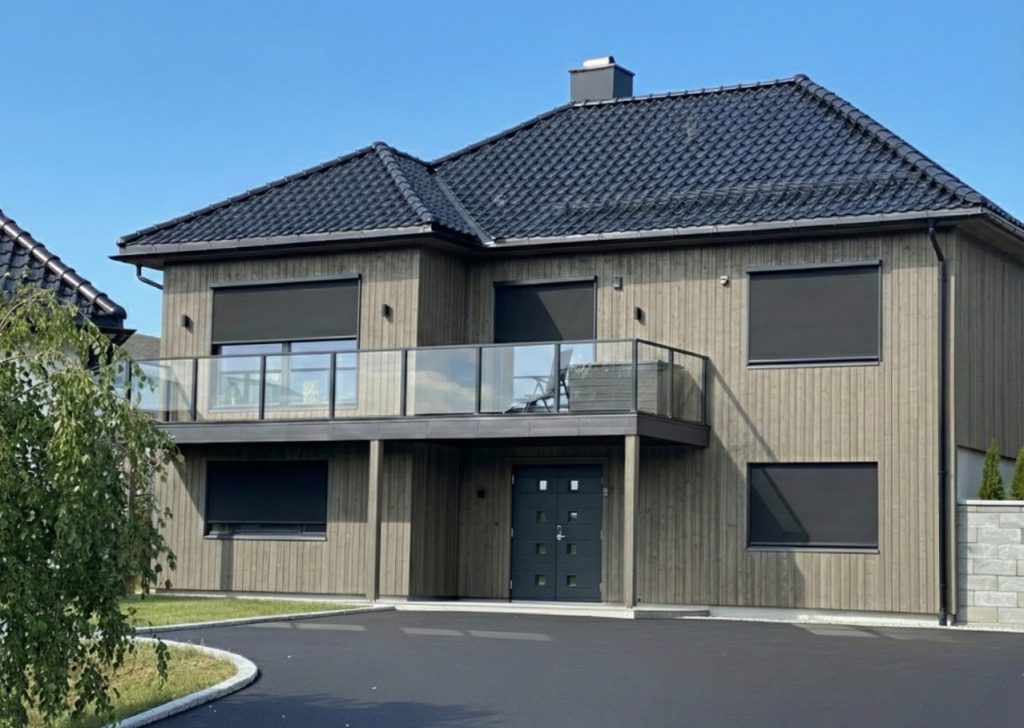 Modern villa med grå träfasad utrustad med flera vertikalmarkiser (zipscreens) i mörk färg på både över- och undervåning.