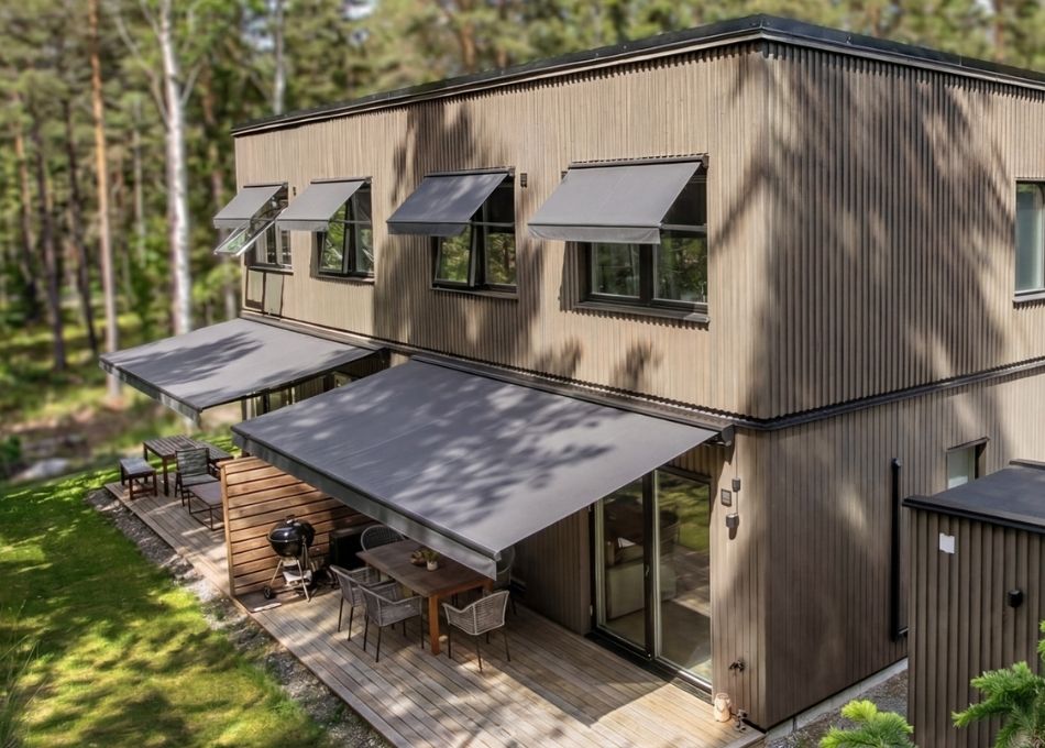 Grå terrassmarkis 3,5 meter med motor, monterad på offwhite hus. Premium solskydd från BILLY Markiser som ger sval skugga över utomhusmatplatsen. Måttanpassad design med slitstark akrylväv och modern elstyrning för bekväm användning.